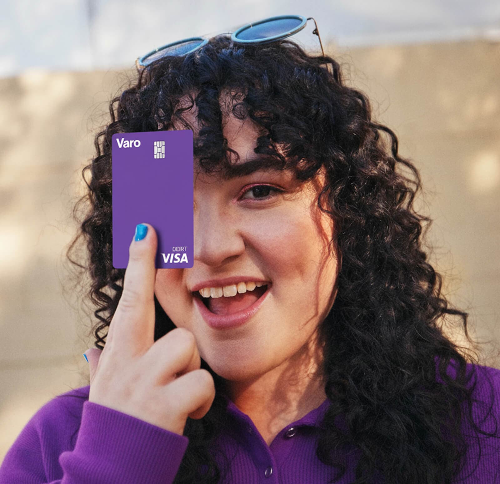 curly haired woman smiling while holding up her Varo Visa debit card